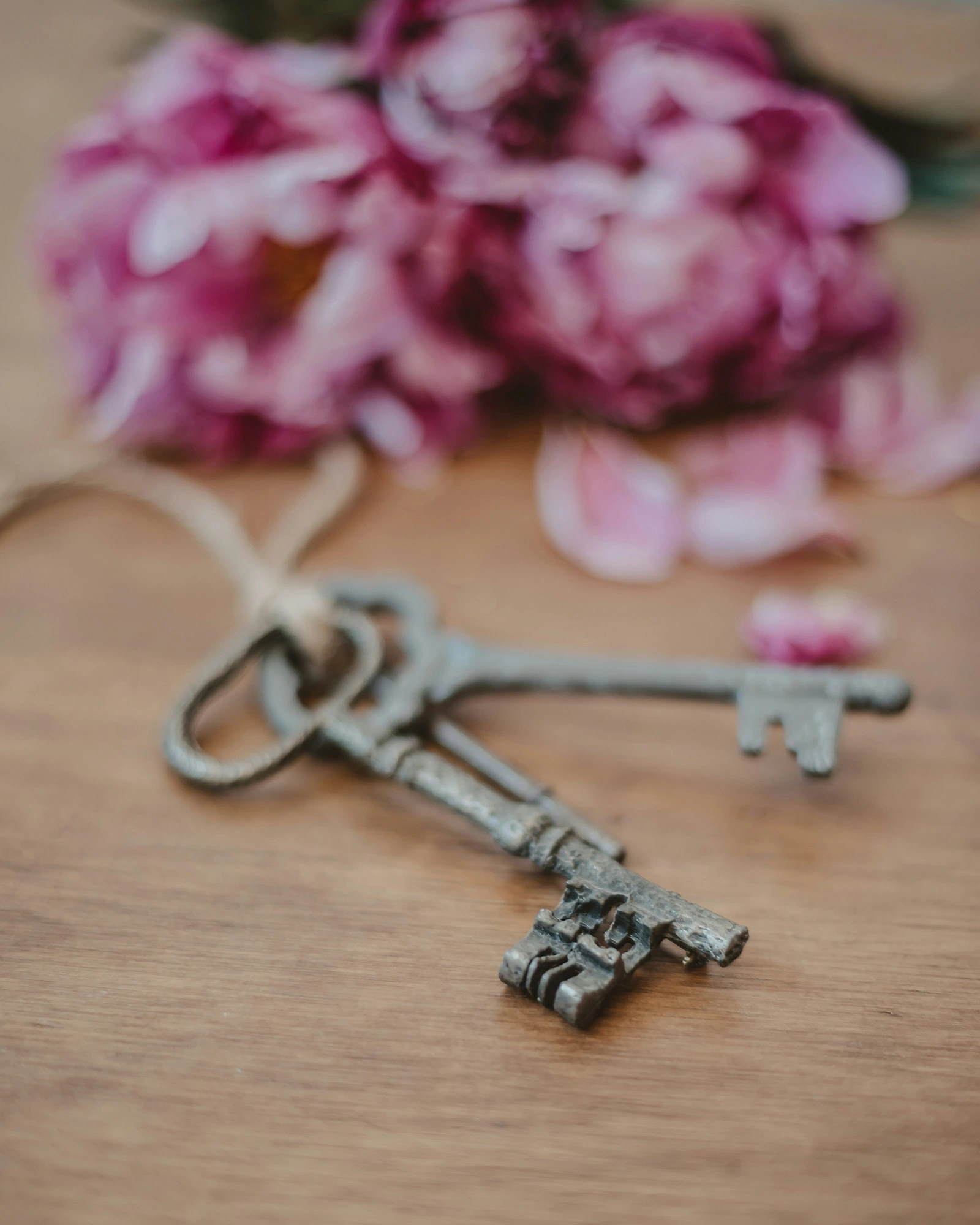 Clés anciennes posées sur une table en bois, devant un bouquet de pivoines